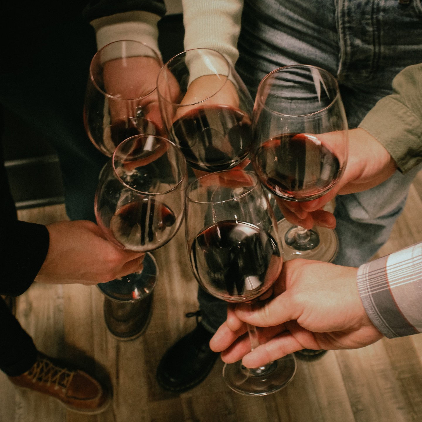 close-up of five individual hands holding partially filled wine glasses make a toast